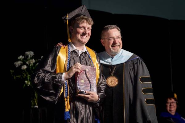 Student holding up award at commencement with President Womack
