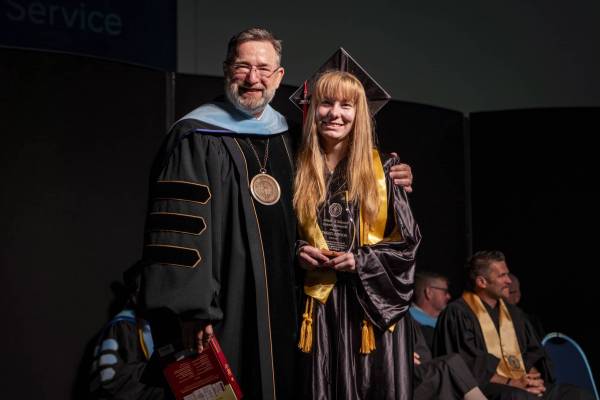 female student holding up award next to president at commencement